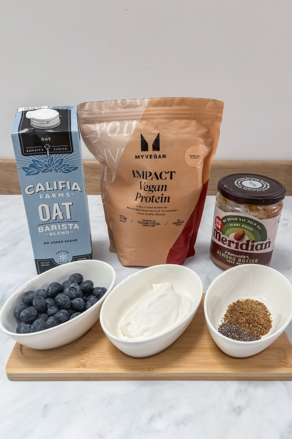 all the ingredients for a high protein blueberry almond butter smoothie. Oat milk, protein powder, almond butter and blueberries